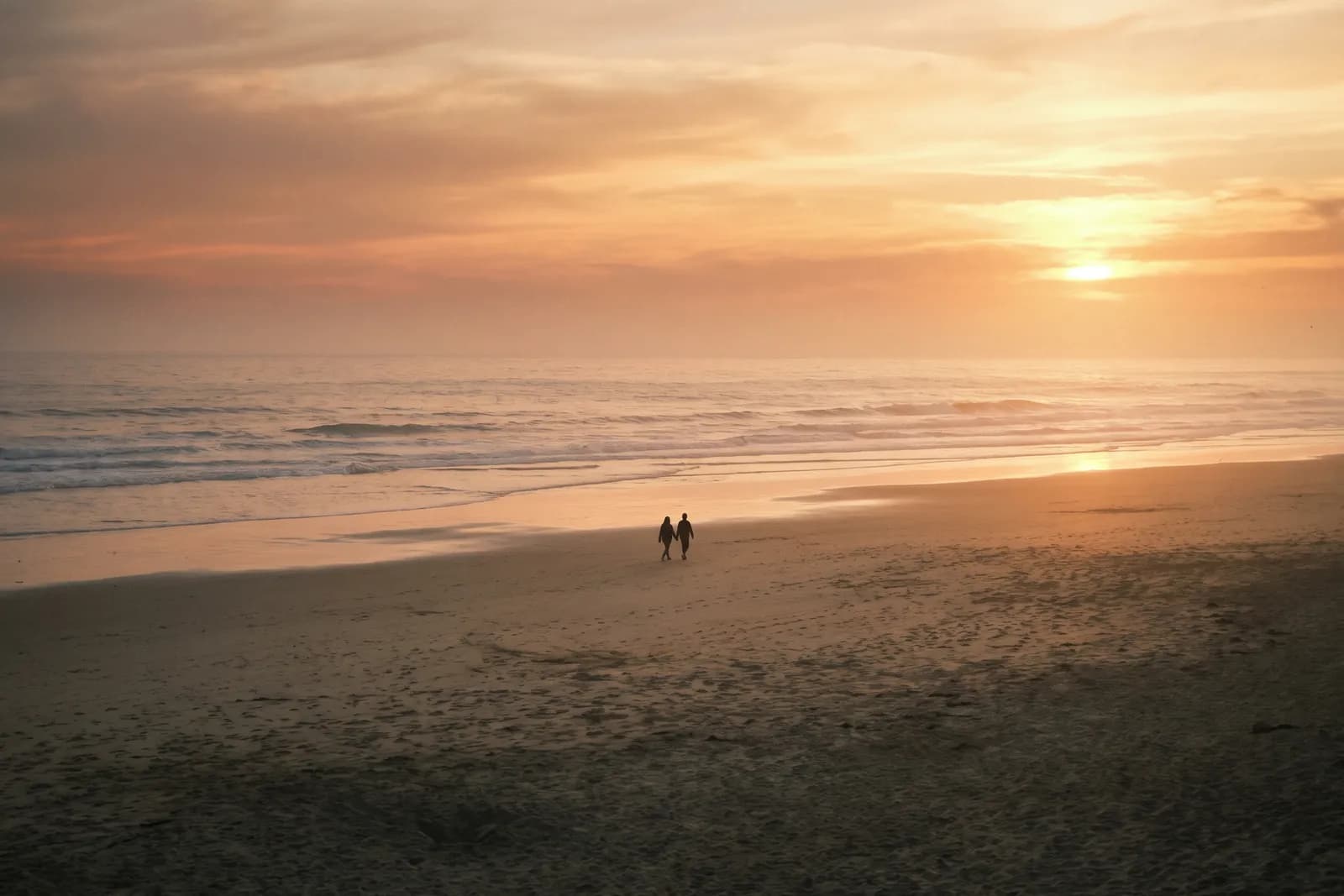 Dos siluetas caminando juntas por la playa al atardecer